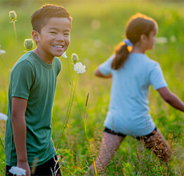 A young boy and girl walking outside together in a field