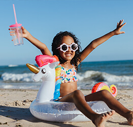 Young girl wearing sunglasses and holding a cup while sitting in a unicorn floatie